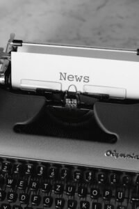 Black and white photo of a classic typewriter with a paper showing the word 'News'.