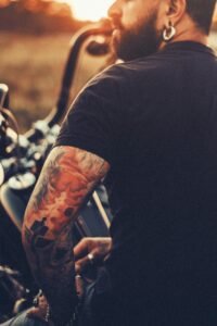 A tattooed motorcyclist enjoying a sunset with a back view profile on a rural road.