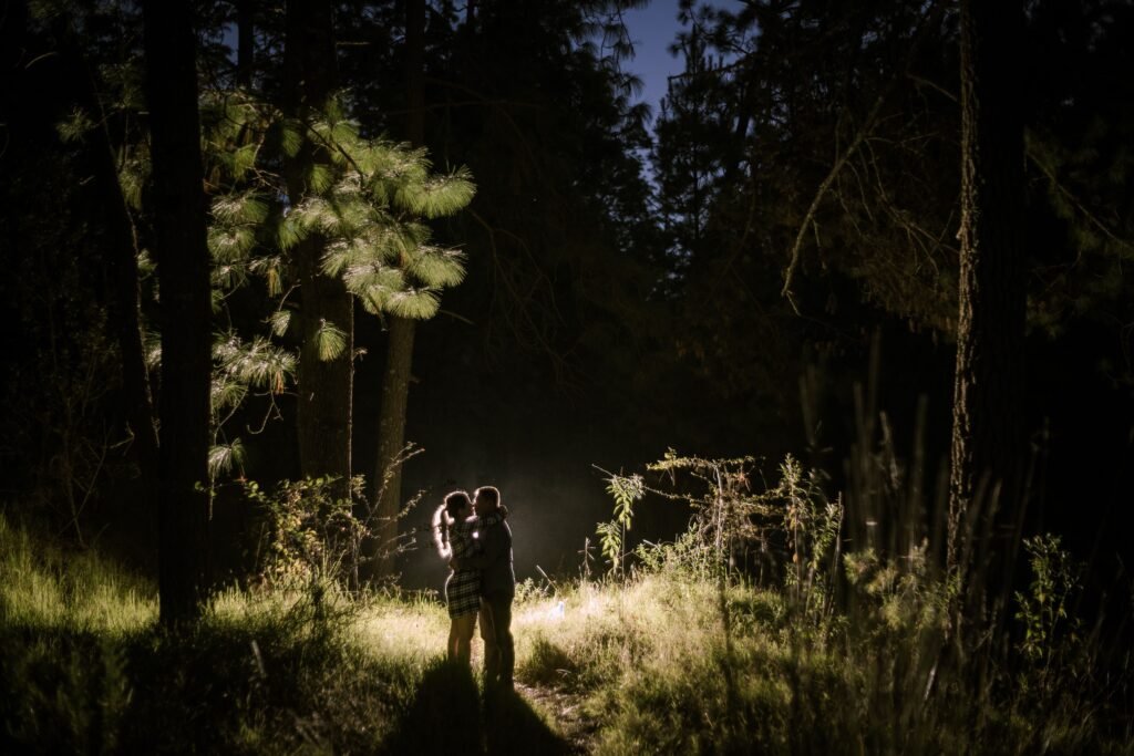 A couple embraces in a dark forest illuminated by moonlight, capturing a moment of love and intimacy.